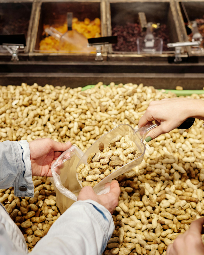 Peanuts being scooped into a bag with other fresh produce visible.