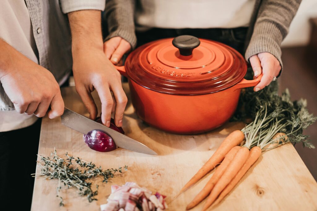 two people preparing a vegetable dish with red onion, carrots, and herbs