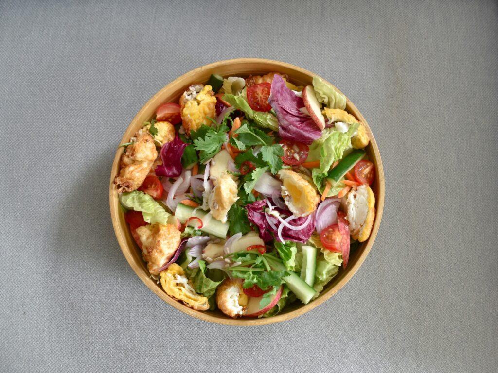 A salad with a mix of fresh produce such as red onion, lettuce, corn and more.