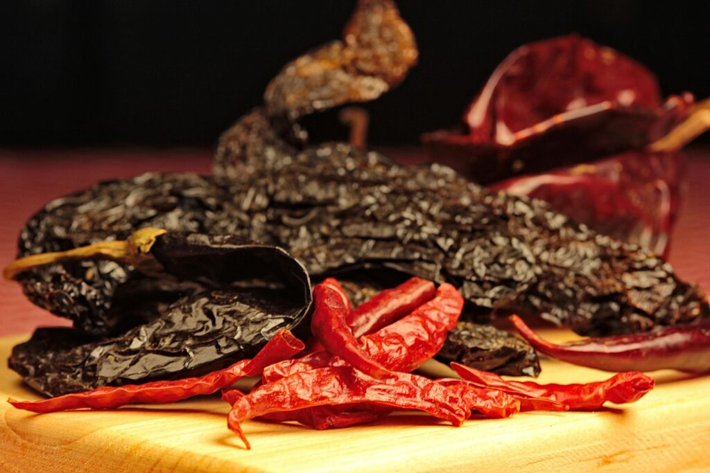 Assorted dried chiles both mild medium and hot spice levels on a wooden board.